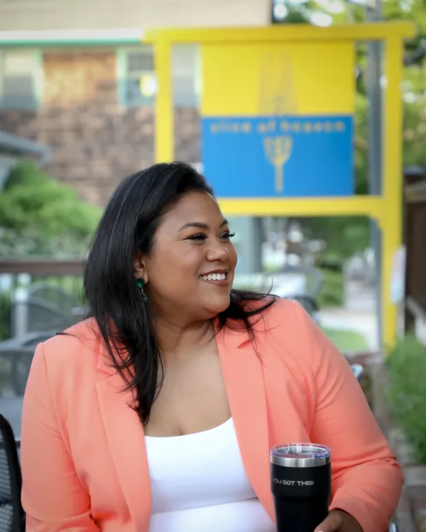 Angela Lima seated at an outdoor table in Newport, smiling and looking off camera