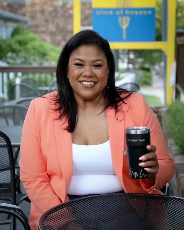 Angela Lima seated outside a Newport cafe holding a travel mug