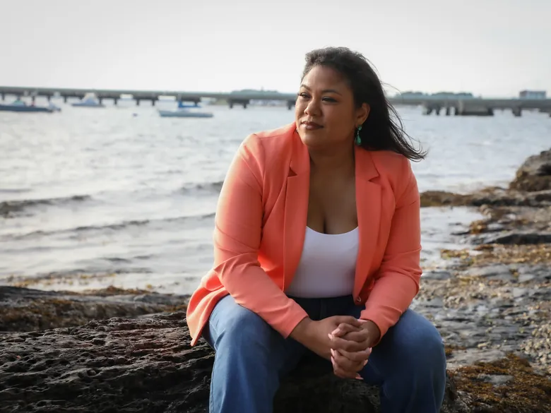 Angela Lima seated on the rocks at the water's edge in Newport, looking out over the bay